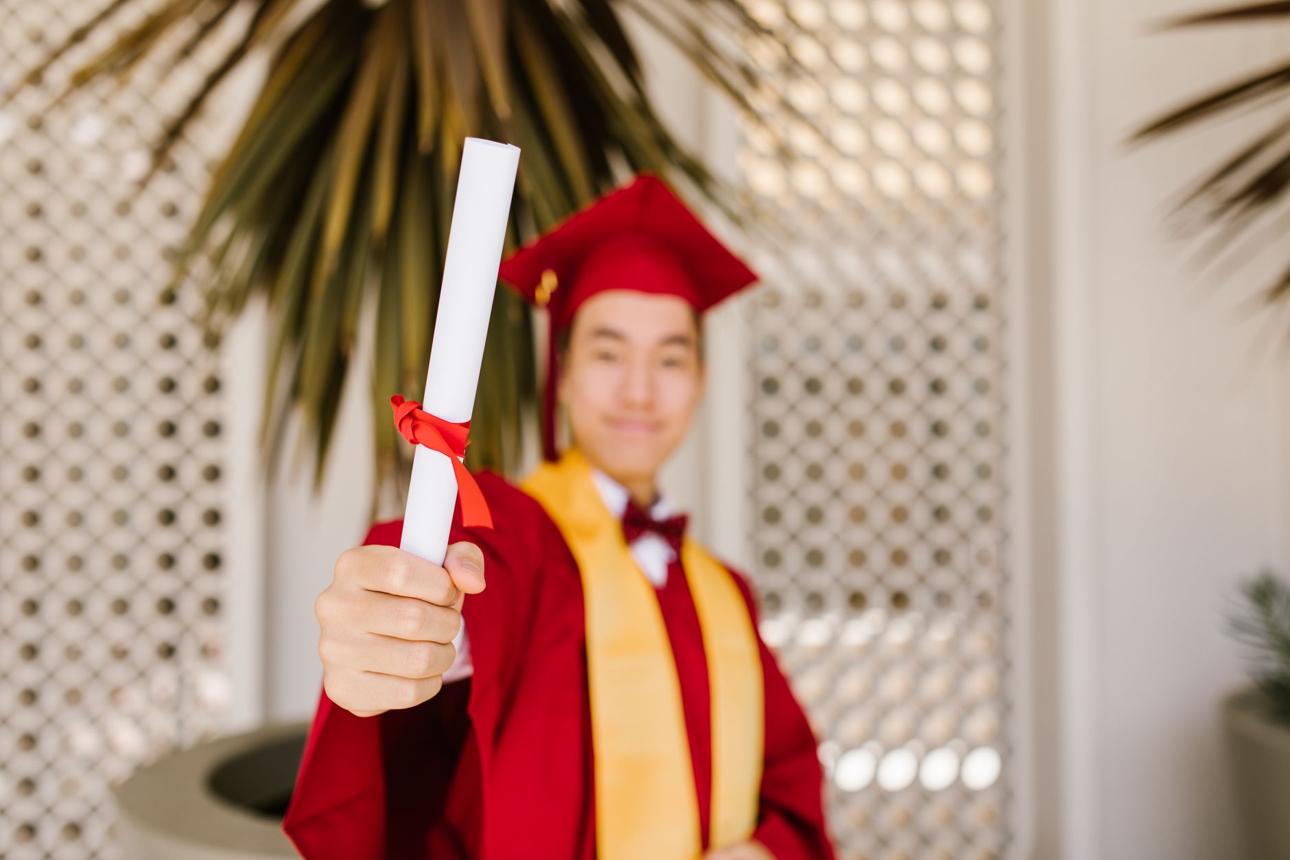 Young graduate in red cap and gown proudly holding diploma, celebrating success.