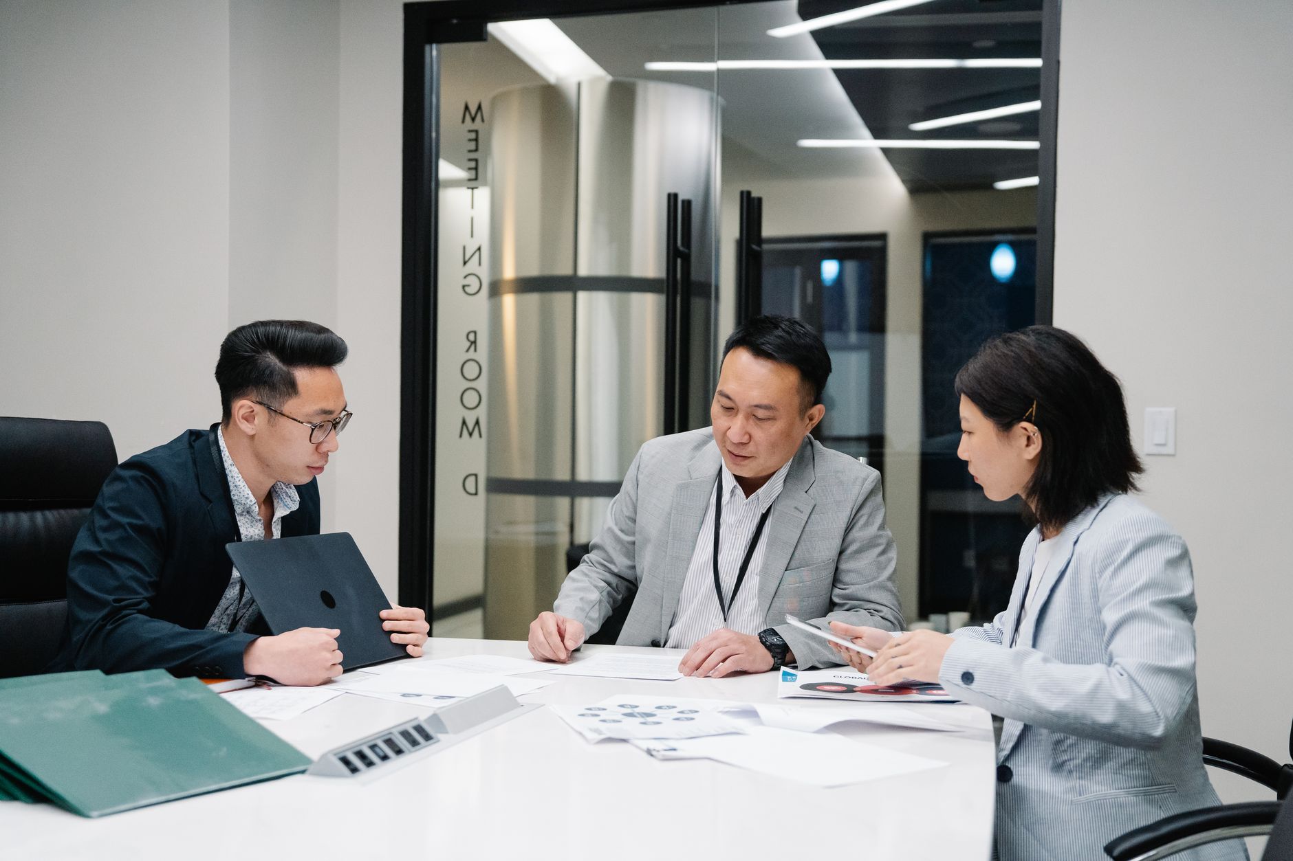 Business meeting with three professionals collaborating in a modern conference room setting.