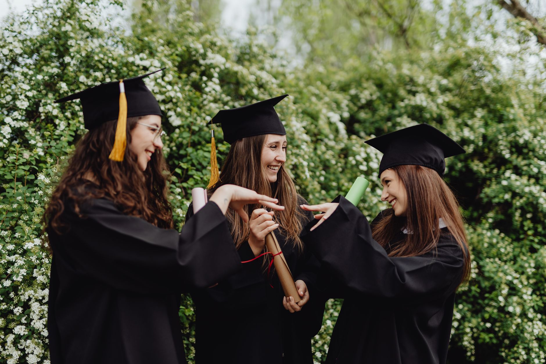 Three female graduates celebrate with diplomas and smiles outdoors.