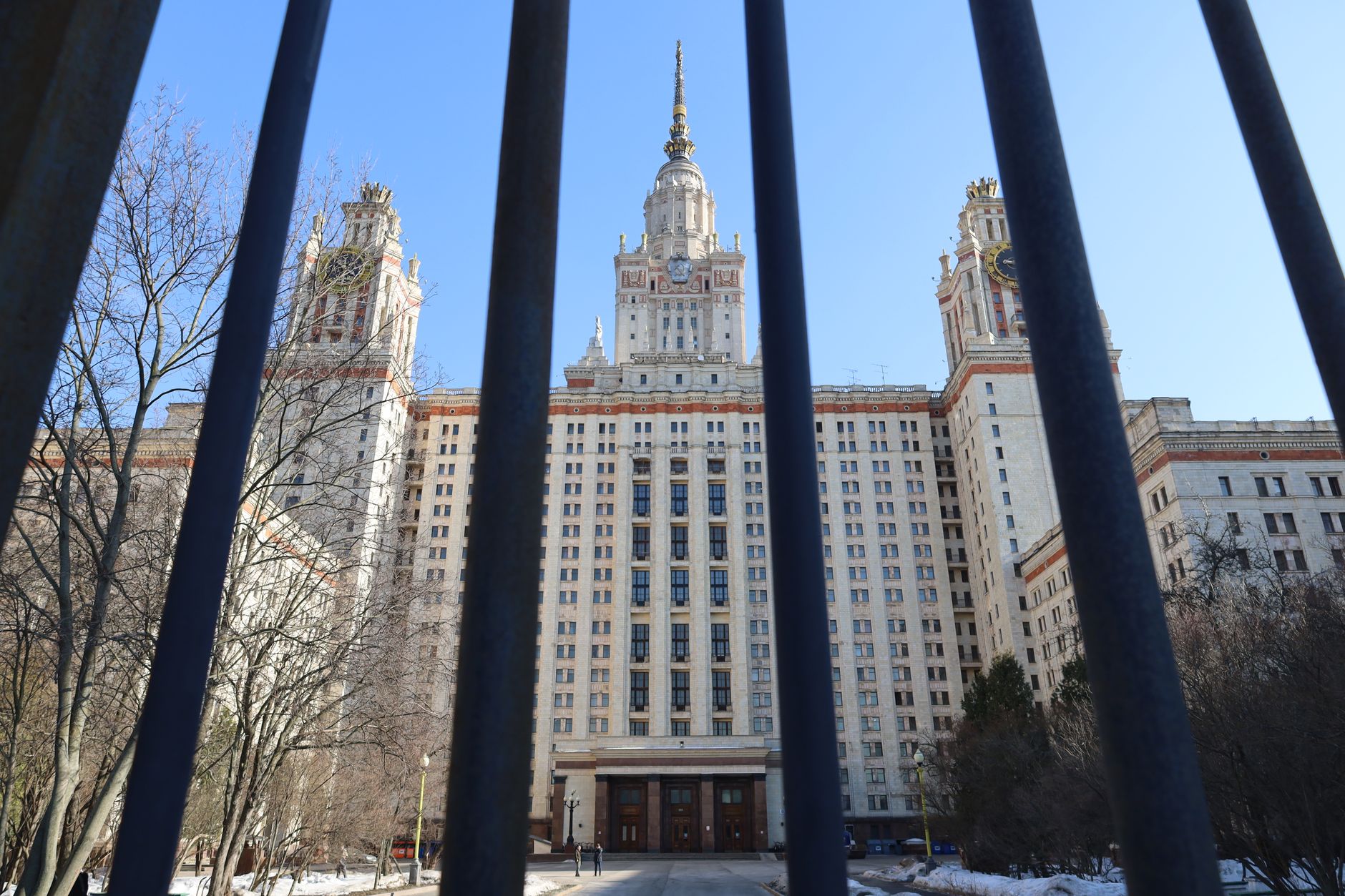 View of the iconic Moscow State University through iron bars on a clear day.