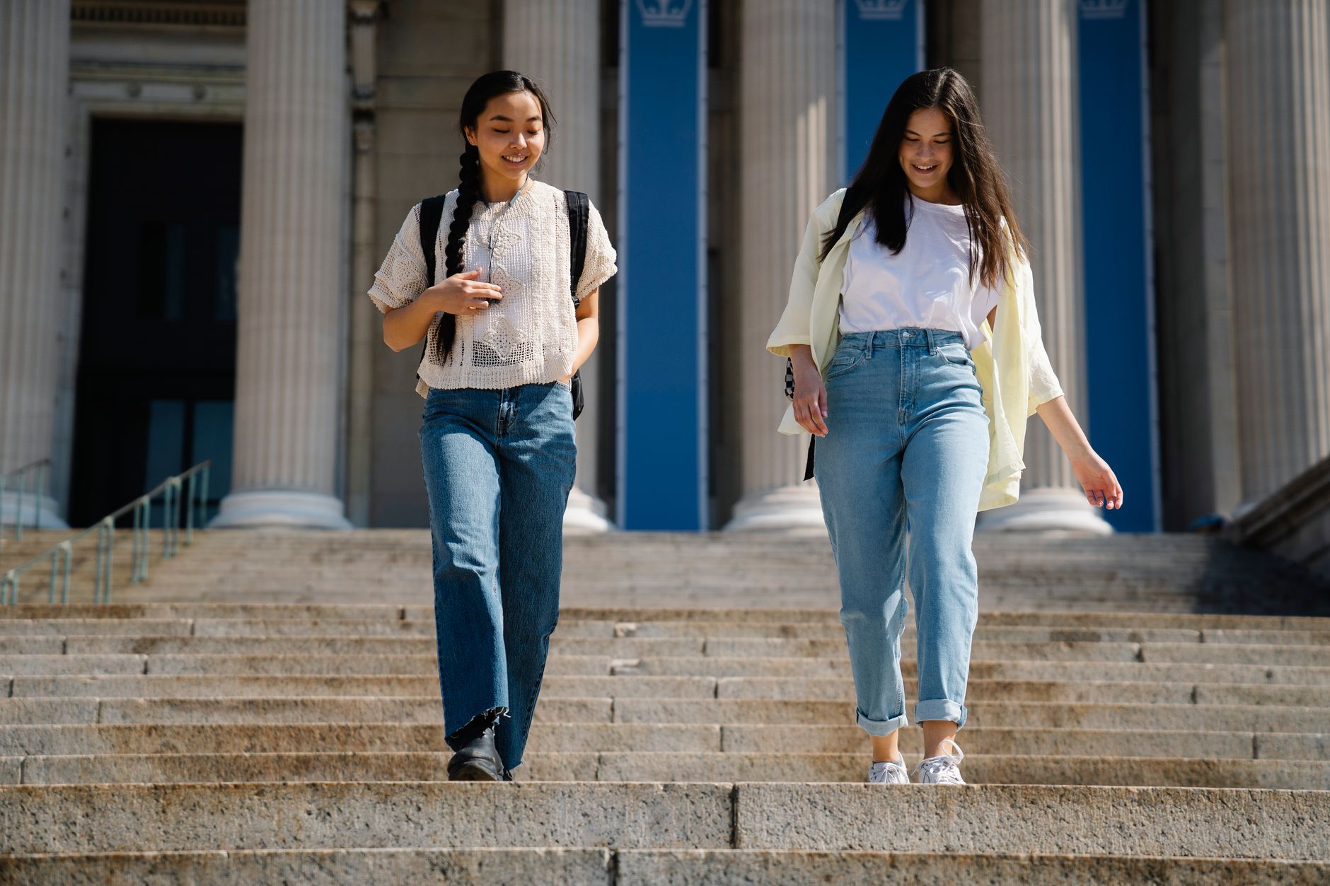Two young women descending stairs outside a historical building, smiling and enjoying the sunny day.